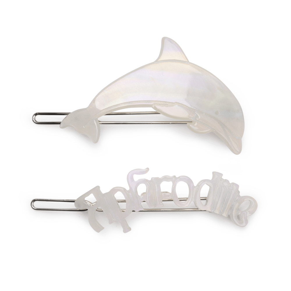 To perlemors hårspænder fra SUI AVA – ét med delfinform og ét med teksten "Aphrodite", begge i en glitrende, hvid akryl og acetat.